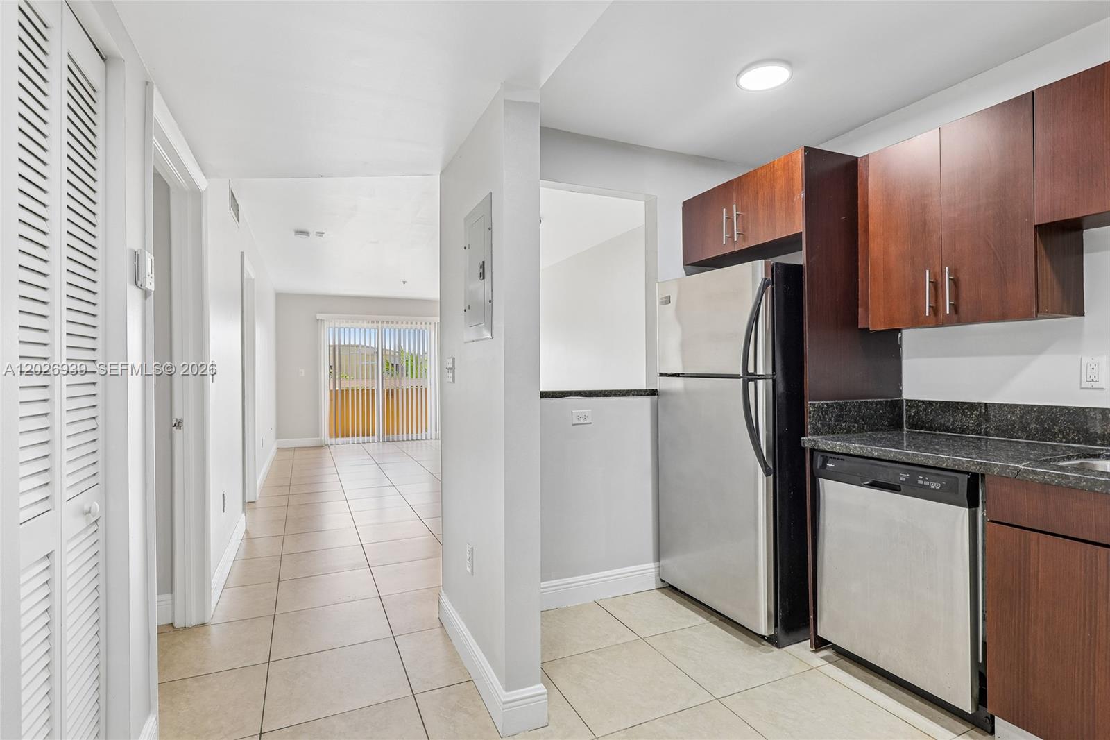 A kitchen with dark wood cabinets and stainless steel appliances opens to a tiled hallway — 4147 Stirling Rd # 504, Dania Beach FL 33314, DANIA BEACH, FL