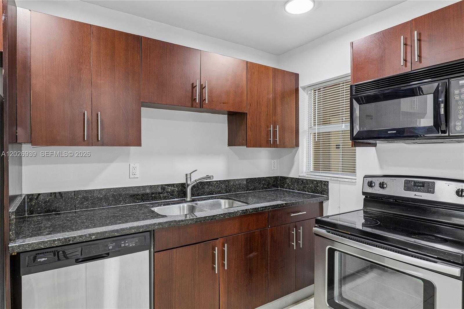 A kitchen features dark wood cabinets, black granite countertops, and stainless steel appliances — 4147 Stirling Rd # 504, Dania Beach FL 33314, DANIA BEACH, FL