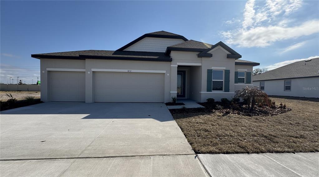 A single-story house with a three-car garage, beige stucco exterior, and a concrete driveway — 857 HAWTHORNE BERRY ROAD, LAKELAND, FL