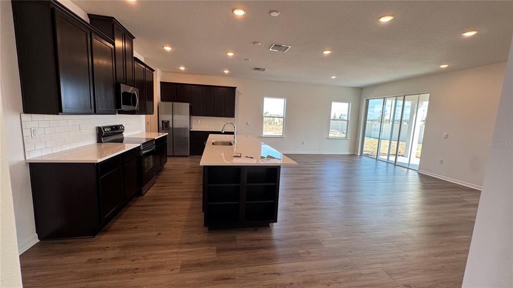 A modern kitchen with dark cabinets, white countertops, and an island opens to a living area — 857 HAWTHORNE BERRY ROAD, LAKELAND, FL