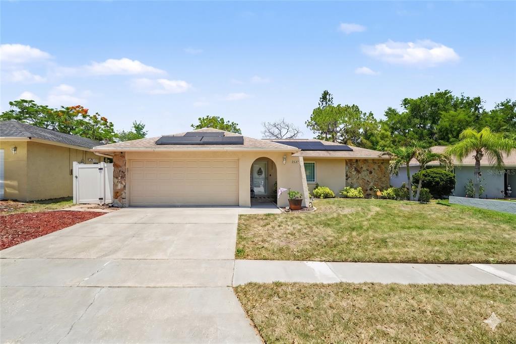 A single-story house with a beige exterior, a two-car garage, and rooftop solar panels — 2627 SURREY DRIVE, PALM HARBOR, FL