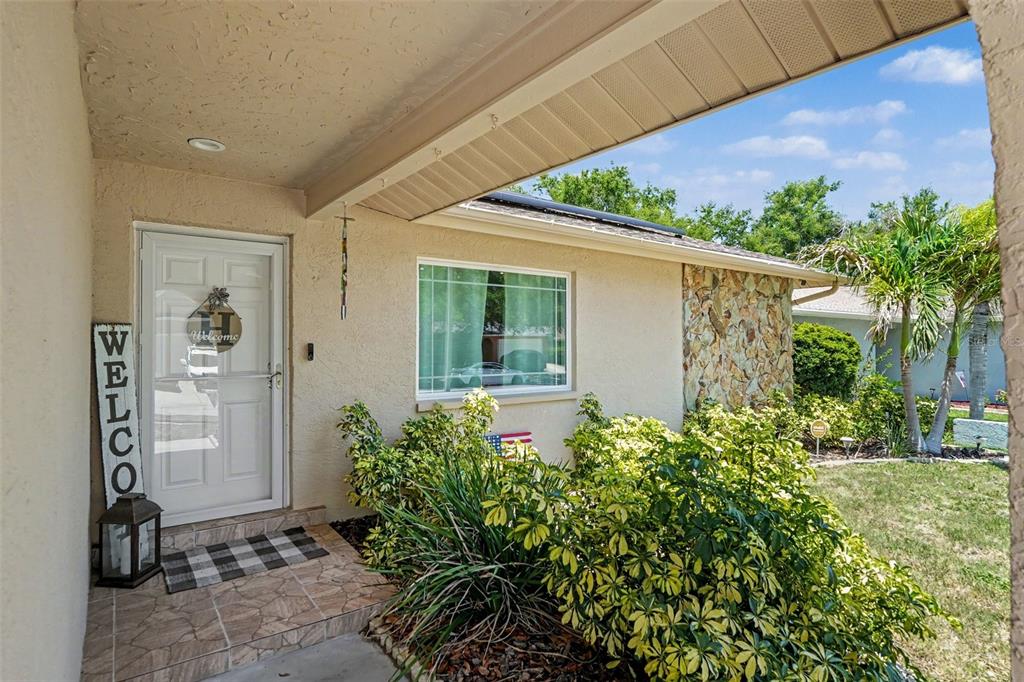 A front entrance features a white door, a welcome sign, and a stone-accented exterior wall — 2627 SURREY DRIVE, PALM HARBOR, FL