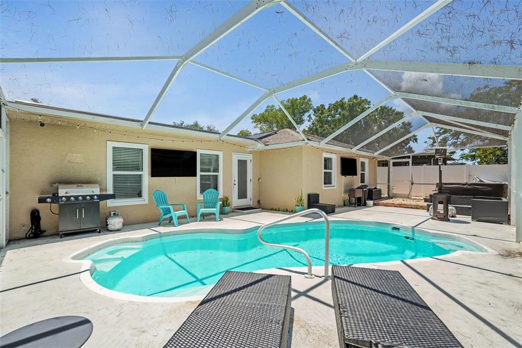 A backyard pool area with a screened-in enclosure, patio furniture, and a grill — 2627 SURREY DRIVE, PALM HARBOR, FL