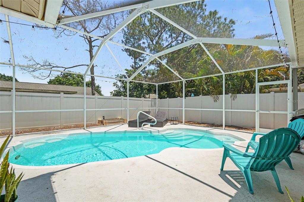 A screened-in swimming pool with a concrete deck and a white vinyl privacy fence — 2627 SURREY DRIVE, PALM HARBOR, FL