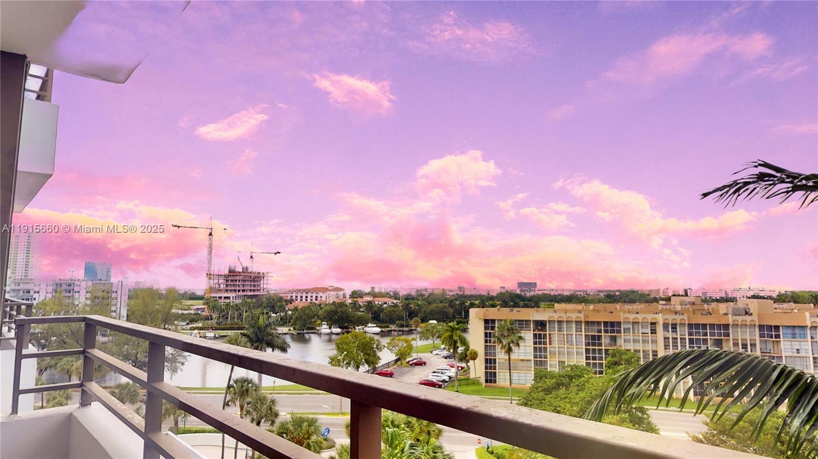 A balcony view overlooking a waterway, parking lot, and buildings under a pink sunset sky — 500 Three Islands Blvd # 408, Hallandale Beach FL 33009, HALLANDALE BEACH, FL