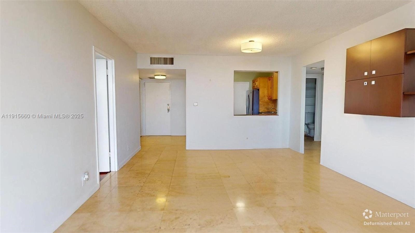 An empty living area features light-colored tile flooring, white walls, and a kitchen pass-through window — 500 Three Islands Blvd # 408, Hallandale Beach FL 33009, HALLANDALE BEACH, FL