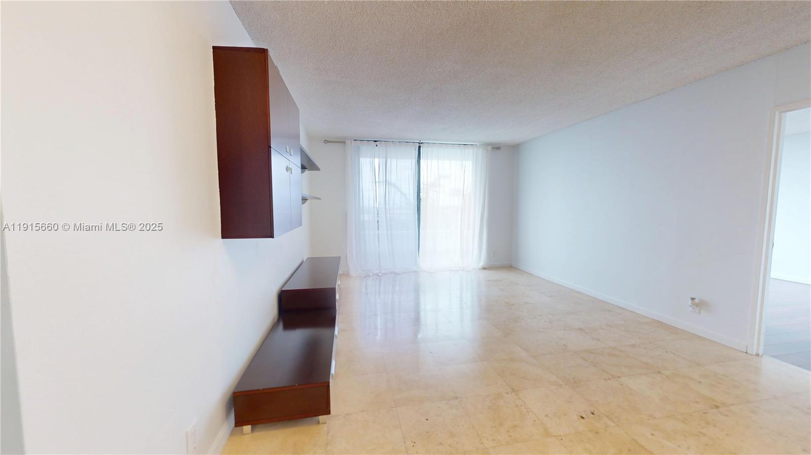 An empty living room features light tile flooring, white walls, and a wall-mounted storage unit — 500 Three Islands Blvd # 408, Hallandale Beach FL 33009, HALLANDALE BEACH, FL