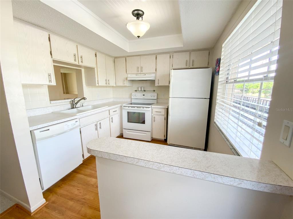 A kitchen features white cabinets, white appliances, a laminate countertop, and a breakfast bar — 1370 HEATHER RIDGE BOULEVARD UNIT 204, DUNEDIN, FL
