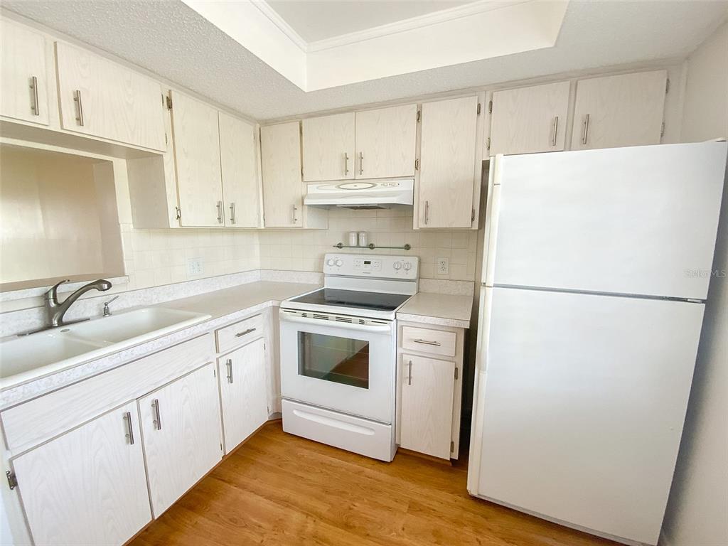 A kitchen features white cabinets, white appliances, a double sink, and light wood-look flooring — 1370 HEATHER RIDGE BOULEVARD UNIT 204, DUNEDIN, FL