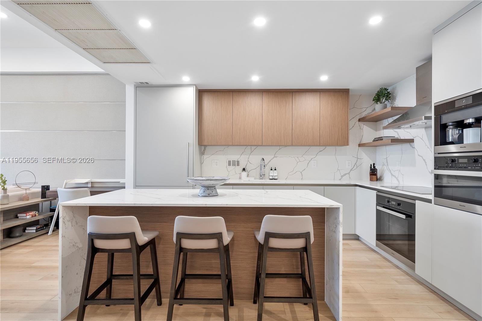 A modern kitchen features a marble-topped island, wood cabinetry, and integrated stainless steel appliances — 2301 Collins Ave # 1633, Miami Beach FL 33139, MIAMI BEACH, FL