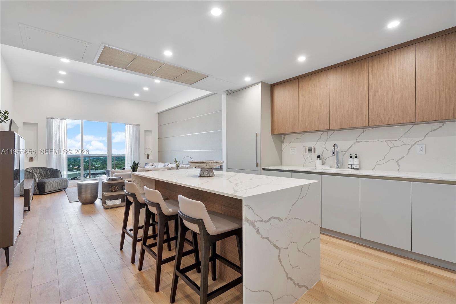 A modern kitchen features a marble waterfall island, light wood cabinetry, and an open living area — 2301 Collins Ave # 1633, Miami Beach FL 33139, MIAMI BEACH, FL
