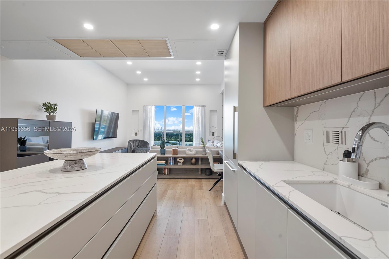 A modern kitchen with white marble countertops and light wood cabinets overlooks a living area — 2301 Collins Ave # 1633, Miami Beach FL 33139, MIAMI BEACH, FL
