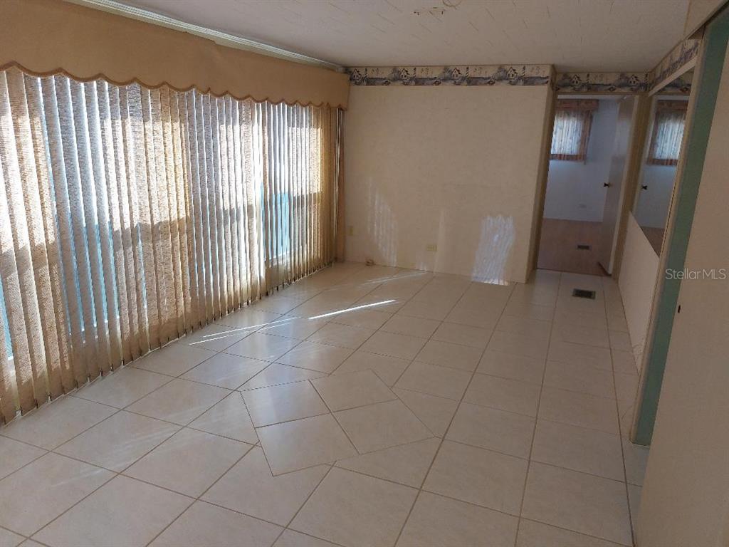 An empty room features light-colored tile flooring, vertical blinds covering a large window, and wallpaper — 269 SALEM AVENUE UNIT 9, PALM HARBOR, FL