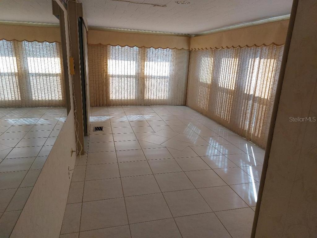 An empty room features white tile flooring, large windows with vertical blinds, and mirrored walls — 269 SALEM AVENUE UNIT 9, PALM HARBOR, FL