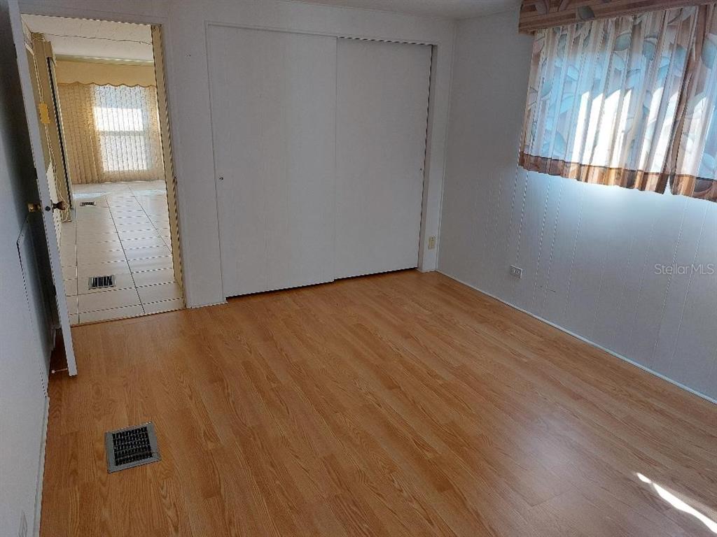 A bedroom with light wood-look flooring, white paneled walls, a sliding closet, and a window — 269 SALEM AVENUE UNIT 9, PALM HARBOR, FL