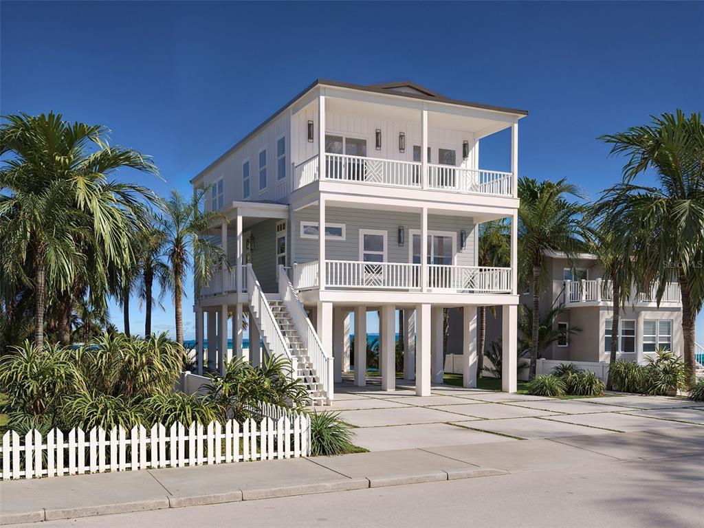 A three-story elevated house with white siding and two levels of covered balconies — 13098 BOCA CIEGA AVENUE, MADEIRA BEACH, FL