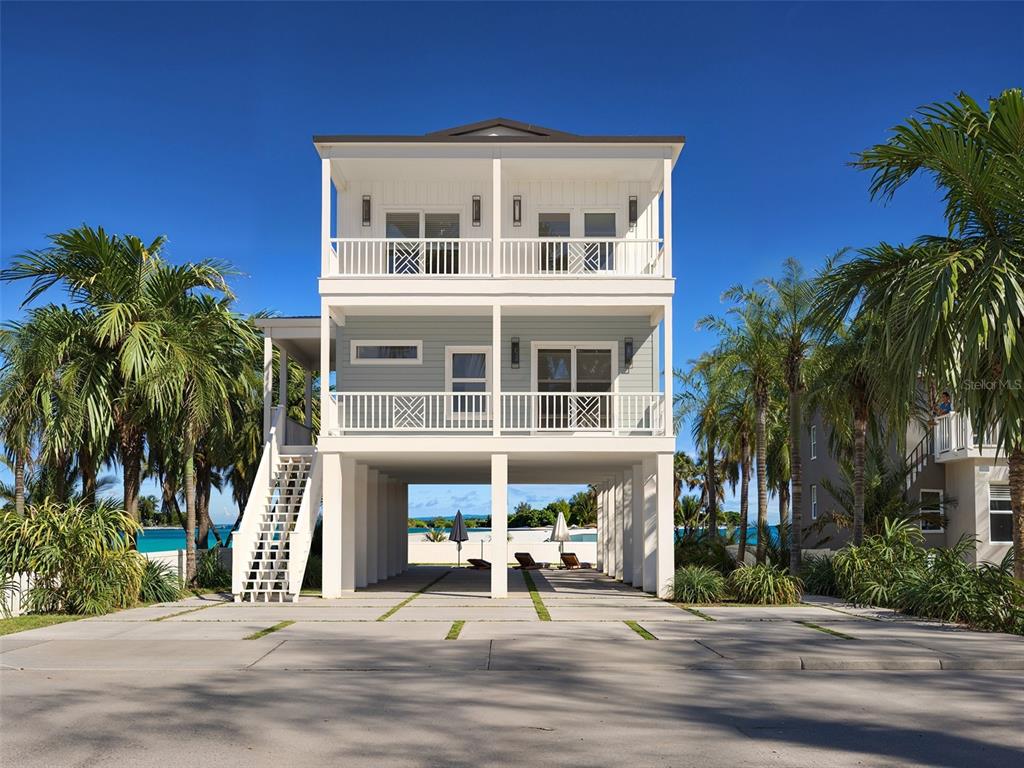 A three-story stilt house with white railings, light blue siding, and a concrete driveway — 13098 BOCA CIEGA AVENUE, MADEIRA BEACH, FL
