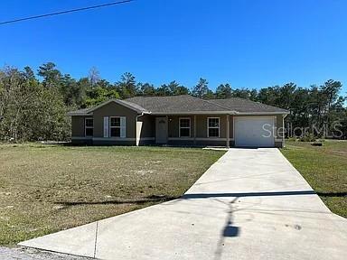 A single-story house with a concrete driveway and a wooded background under a clear sky — 17184 SW 44TH CIRCLE, OCALA, FL