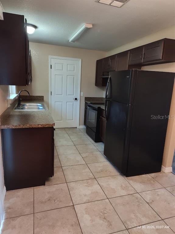 A kitchen features dark wood cabinets, black appliances, a double sink, and light-colored tile flooring — 17184 SW 44TH CIRCLE, OCALA, FL