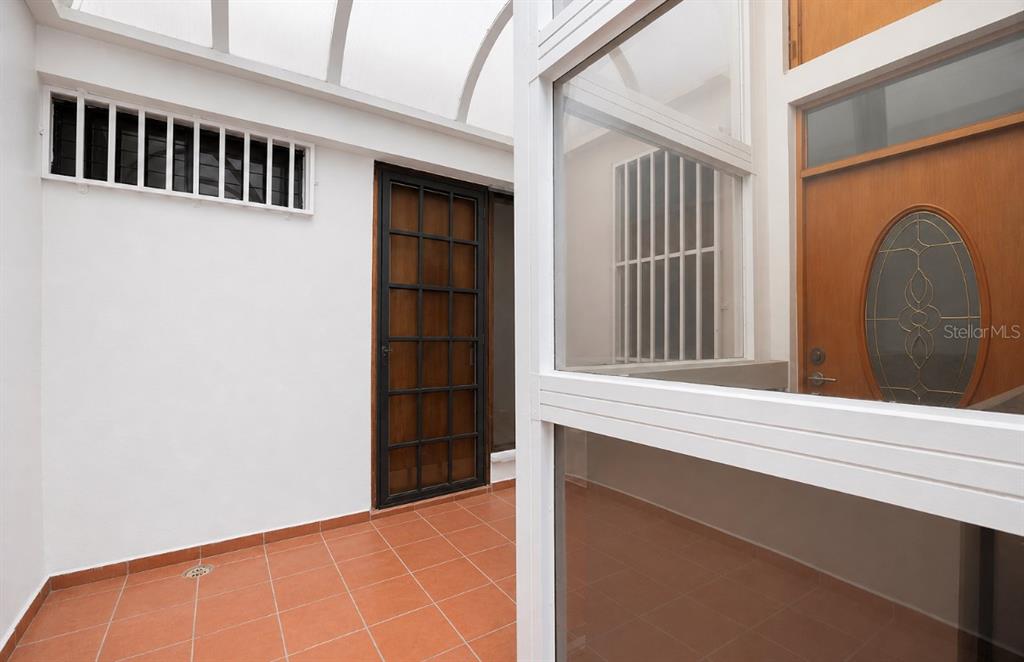 A tiled entryway features a glass-paneled roof, a wooden door, and a metal security gate — B-14 CALLE SEVILLA BILTMORE, GUAYNABO, PR