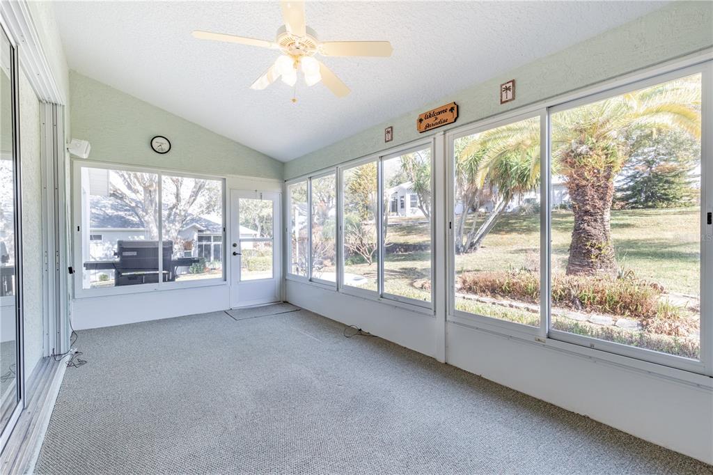 A living room with light wood floors, patterned sofas, a wooden entertainment center, and kitchen bar — 5732 FREEPORT DRIVE, TAVARES, FL