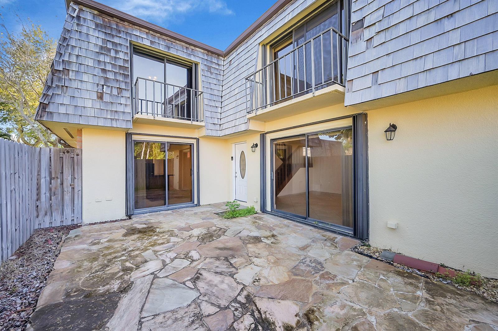 A stone patio sits in front of a two-story house with sliding glass doors and balconies — 128 Lake Arbor Drive, Palm Springs FL 33461, PALM SPRINGS, FL