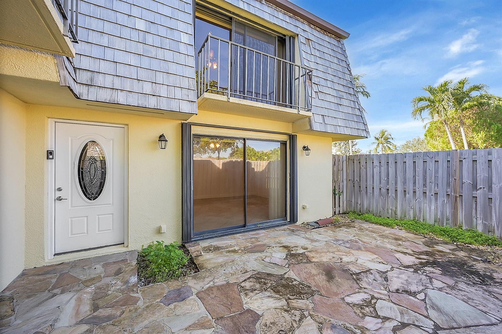 A stone patio sits in front of a house with a white door and balcony — 128 Lake Arbor Drive, Palm Springs FL 33461, PALM SPRINGS, FL