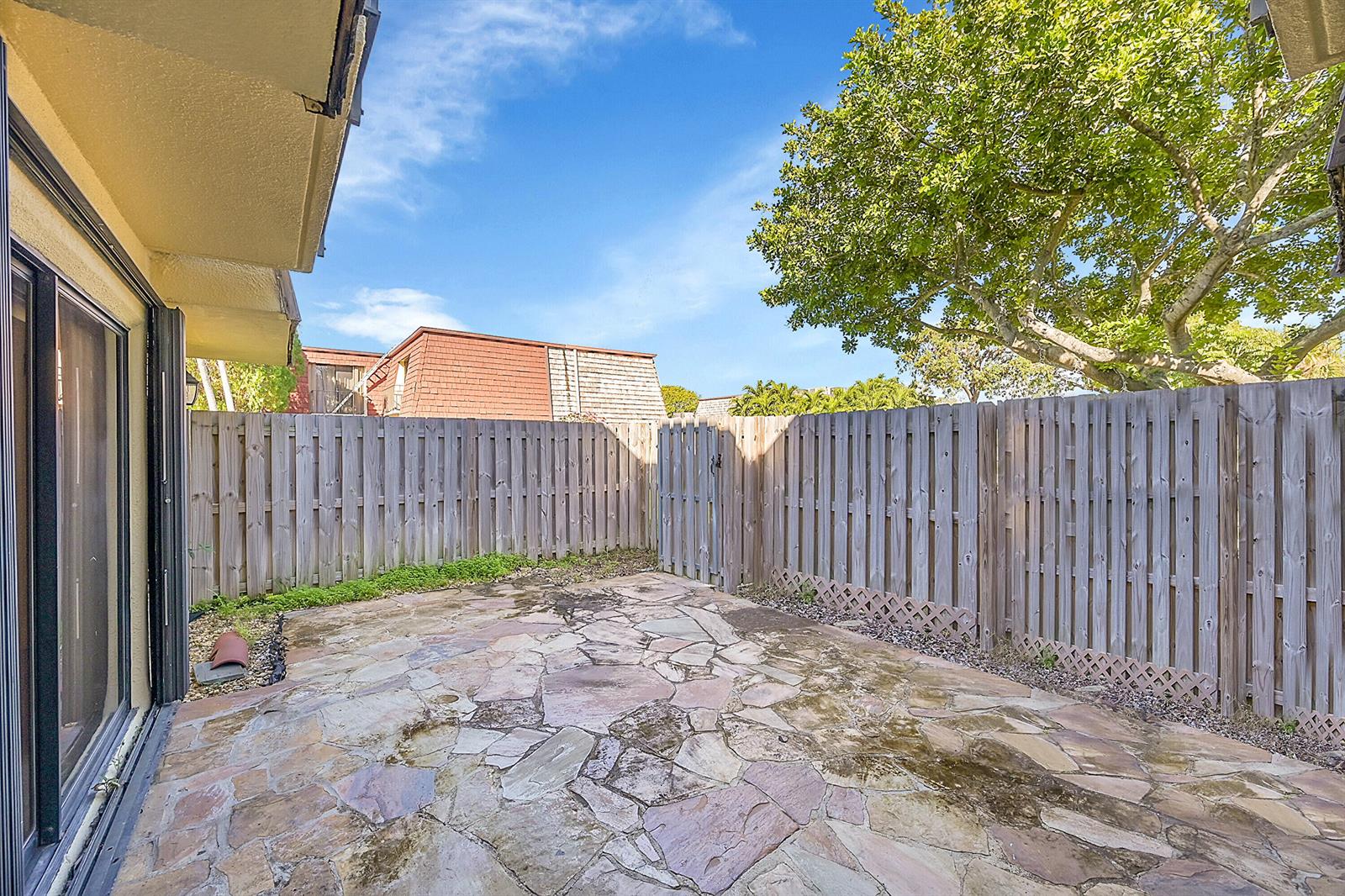 A stone patio sits enclosed by a wooden fence with a large tree overhead — 128 Lake Arbor Drive, Palm Springs FL 33461, PALM SPRINGS, FL
