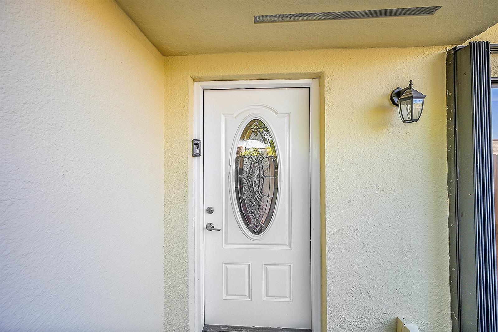 A white front door with an oval glass insert is set in a yellow wall — 128 Lake Arbor Drive, Palm Springs FL 33461, PALM SPRINGS, FL