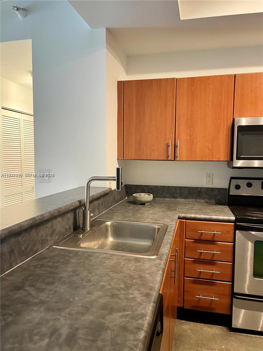 A kitchen features wood cabinets, a stainless steel sink, and dark gray laminate countertops — 455 NE 25th St # 407, Miami FL 33137, MIAMI, FL
