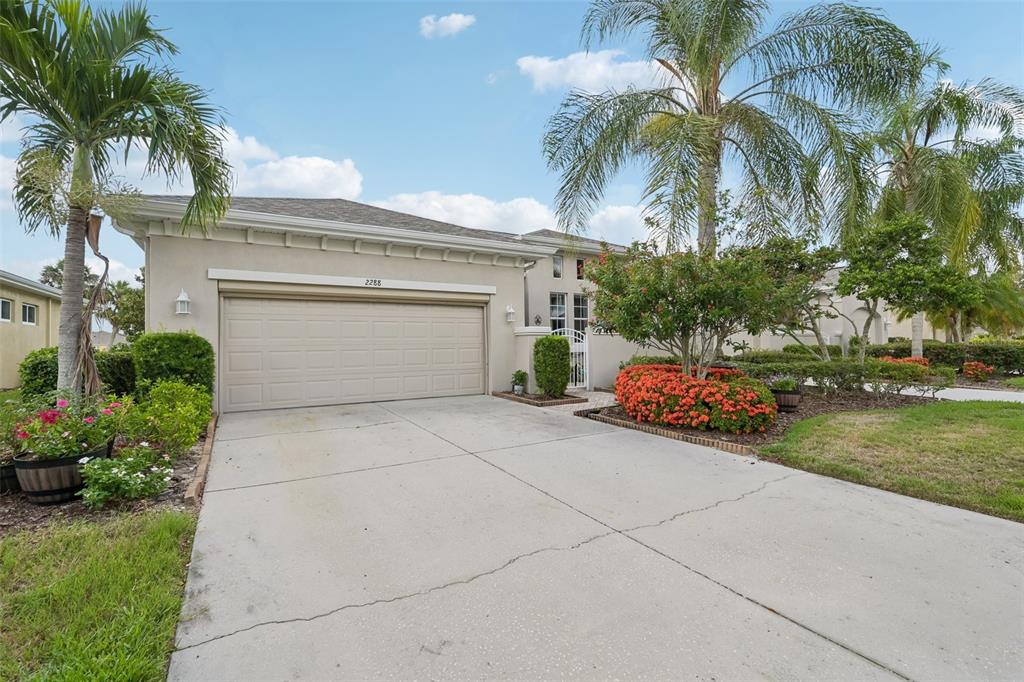 A beige house with a two-car garage, palm trees, and a concrete driveway — 2288 SIFIELD GREENS WAY, SUN CITY CENTER, FL