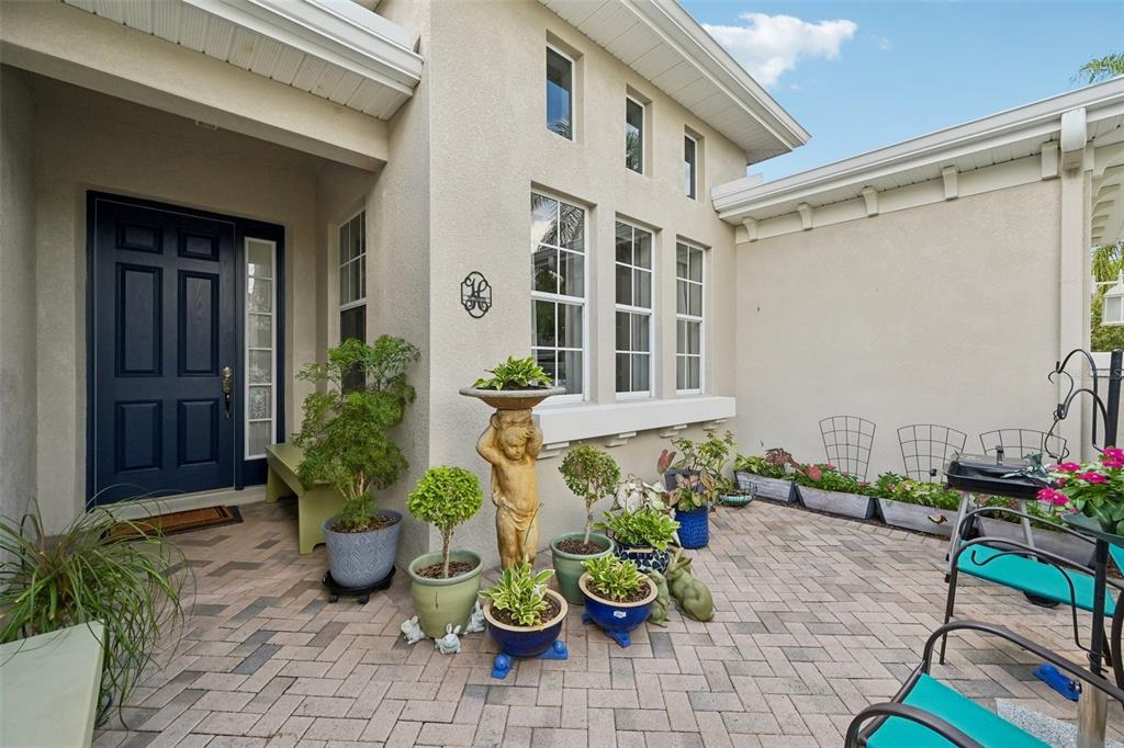 A paved patio area features a dark blue front door and several potted plants — 2288 SIFIELD GREENS WAY, SUN CITY CENTER, FL