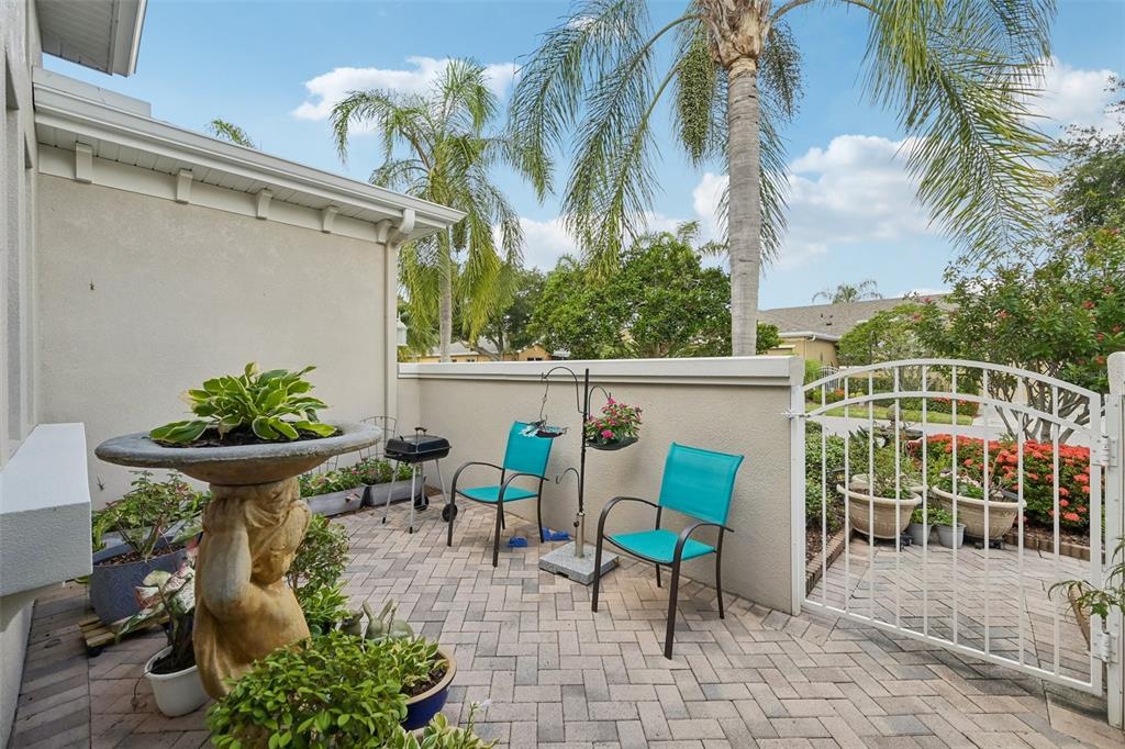 A paved patio features a birdbath, two teal chairs, a small grill, and a white gate — 2288 SIFIELD GREENS WAY, SUN CITY CENTER, FL