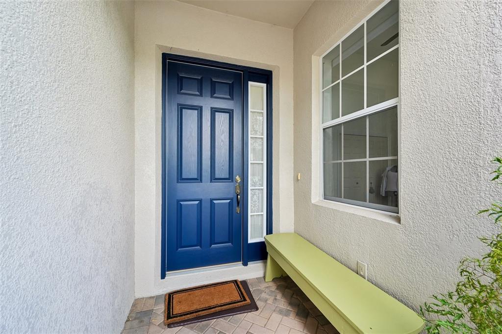 A blue front door with a sidelight and a green bench on a paved porch — 2288 SIFIELD GREENS WAY, SUN CITY CENTER, FL