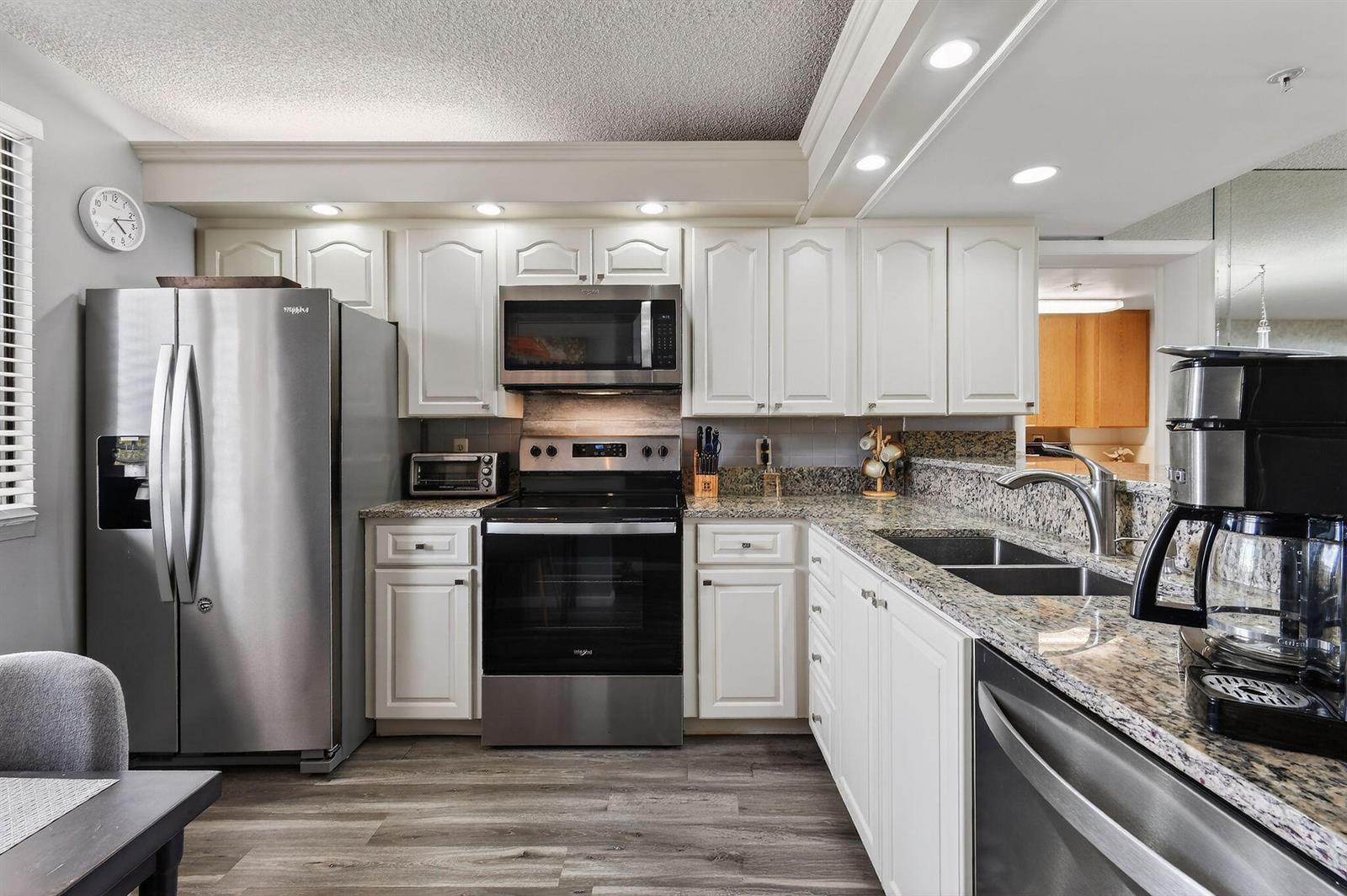 A kitchen featuring white cabinets, granite countertops, stainless steel appliances, and wood-look flooring — 2401 Marina Isle Way # 206, Jupiter FL 33477, JUPITER, FL
