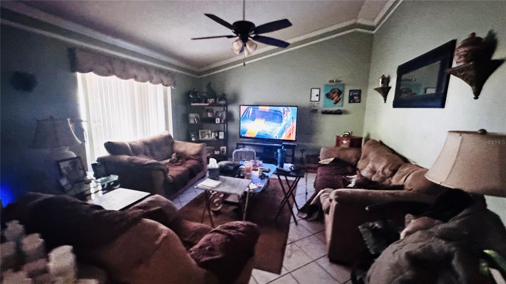 A living room features brown sofas, a ceiling fan, a television, and tile flooring — 8168 STRADA DRIVE, ORLANDO, FL