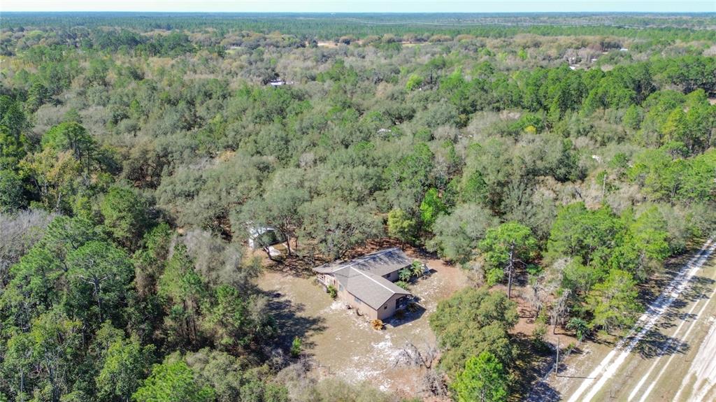 An aerial view shows a house nestled in a wooded lot near a dirt road — 13455 NE 228TH LANE ROAD, FORT MC COY, FL