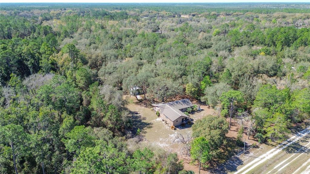 An aerial view shows a single-story house surrounded by dense woods and a dirt driveway — 13455 NE 228TH LANE ROAD, FORT MC COY, FL