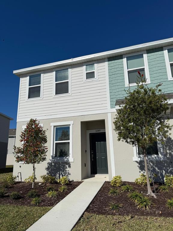 A two-story townhouse exterior features light-colored siding, a dark front door, and two small trees — 3208 SKYLINE LOOP, KISSIMMEE, FL