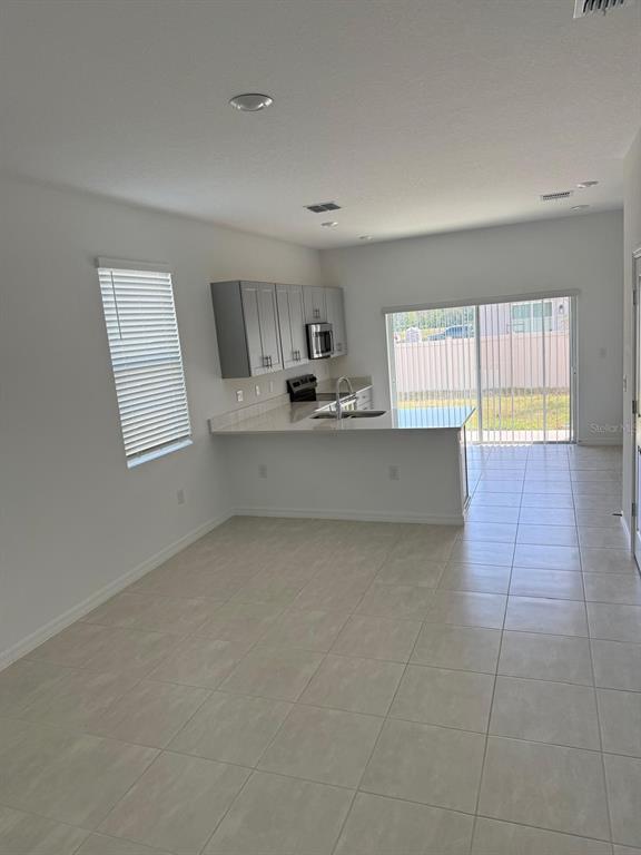 A kitchen with grey cabinets and a breakfast bar overlooks a tiled living area — 3208 SKYLINE LOOP, KISSIMMEE, FL