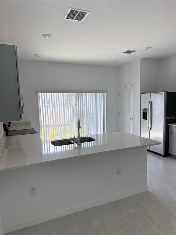 A kitchen with a white quartz island, stainless steel refrigerator, and sliding glass doors — 3208 SKYLINE LOOP, KISSIMMEE, FL