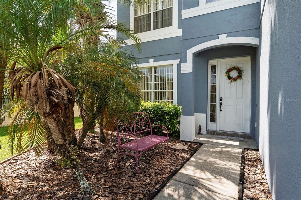 A pink metal bench sits on mulch in front of a blue house entrance — 2232 WINDCREST LAKE CIRCLE, ORLANDO, FL