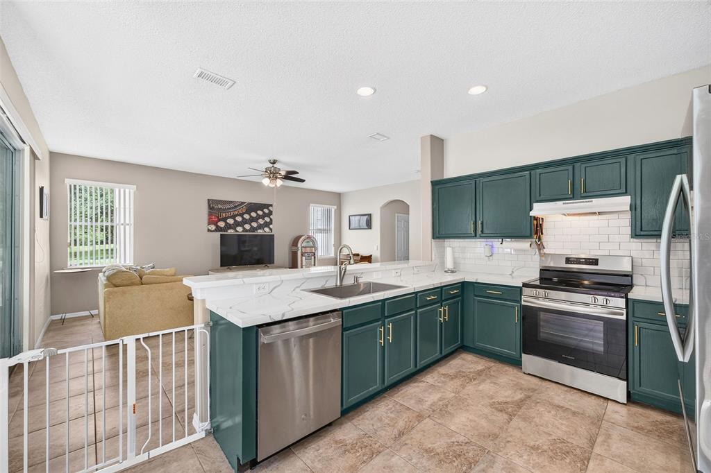 A kitchen with dark green cabinets, white countertops, and stainless steel appliances overlooks a living room — 2232 WINDCREST LAKE CIRCLE, ORLANDO, FL