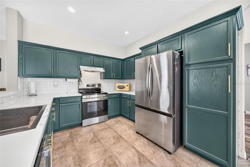 A kitchen features dark green cabinets, stainless steel appliances, white countertops, and tile flooring — 2232 WINDCREST LAKE CIRCLE, ORLANDO, FL