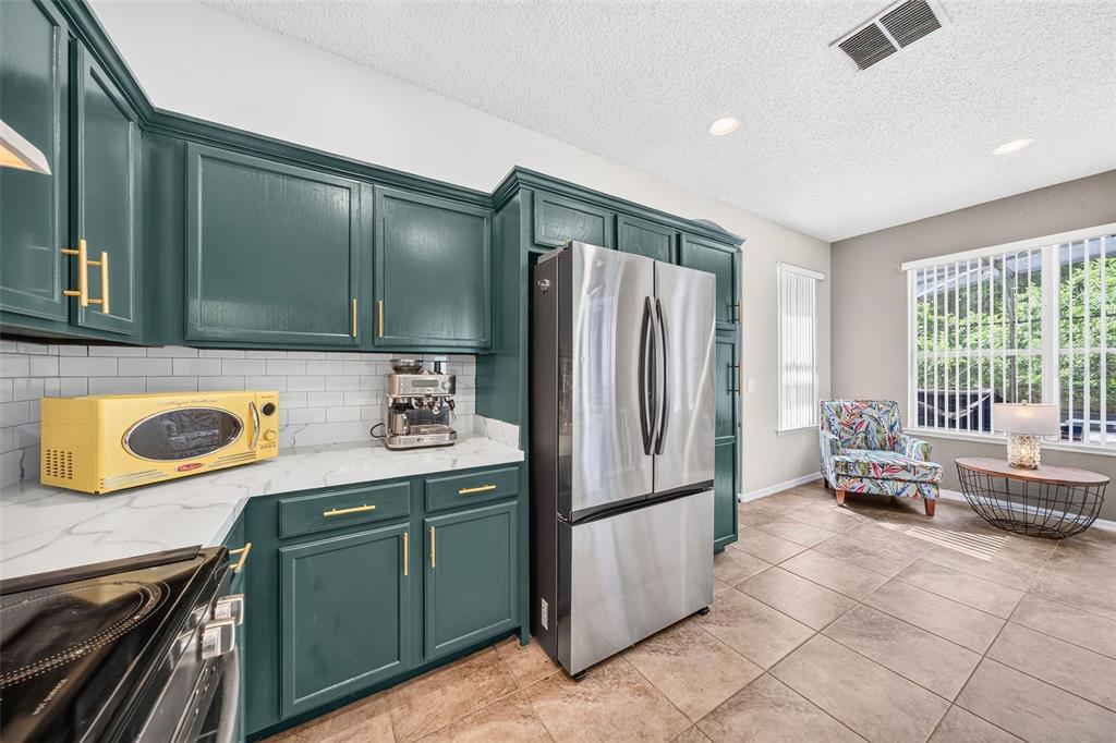 A kitchen features dark green cabinets, stainless steel appliances, and a small seating area nearby — 2232 WINDCREST LAKE CIRCLE, ORLANDO, FL