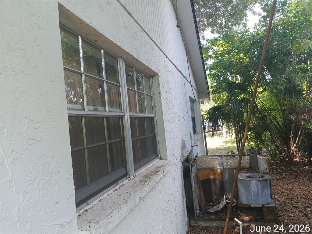An exterior view of a white stucco wall with windows and a damaged HVAC unit — 7203 N 41ST STREET, TAMPA, FL