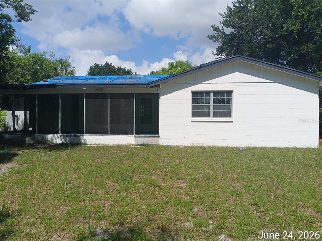 The exterior of a single-story house features a screened-in porch and a blue tarp roof — 7203 N 41ST STREET, TAMPA, FL