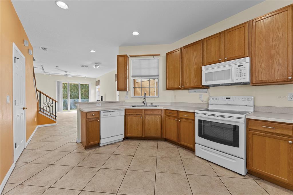 A kitchen with wood cabinets, white appliances, and tile flooring opens to a living area — 1938 FIESTA RIDGE COURT, TAMPA, FL
