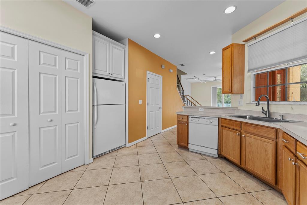 A kitchen features wood cabinets, white appliances, tile flooring, and an adjacent orange-walled hallway — 1938 FIESTA RIDGE COURT, TAMPA, FL