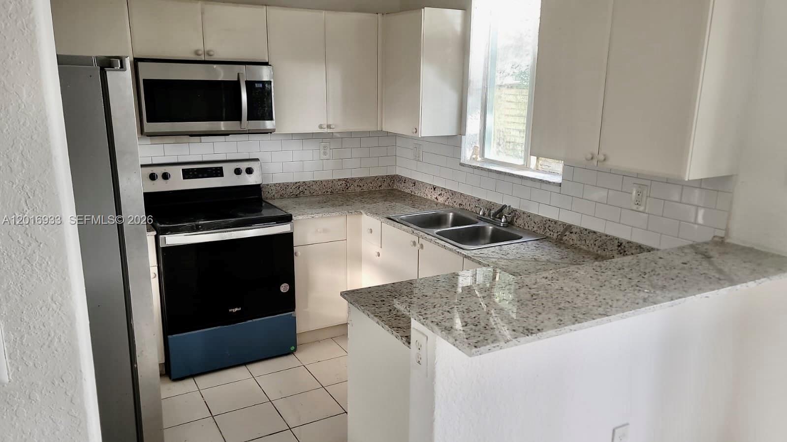 A kitchen features white cabinets, granite countertops, stainless steel appliances, and a subway tile backsplash — HOMESTEAD, FL